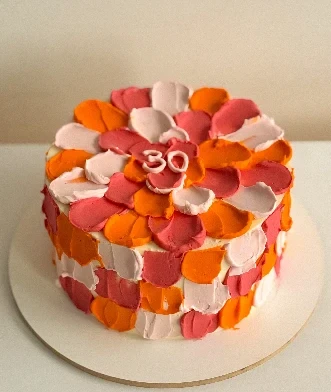 Bolo coberto de pétalas de buttercream em vermelho, laranja e rosa